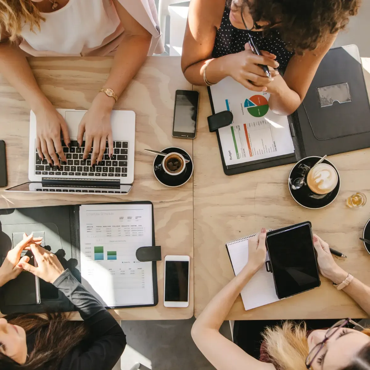 Top view of 4 people working at a table with coffees and laptops