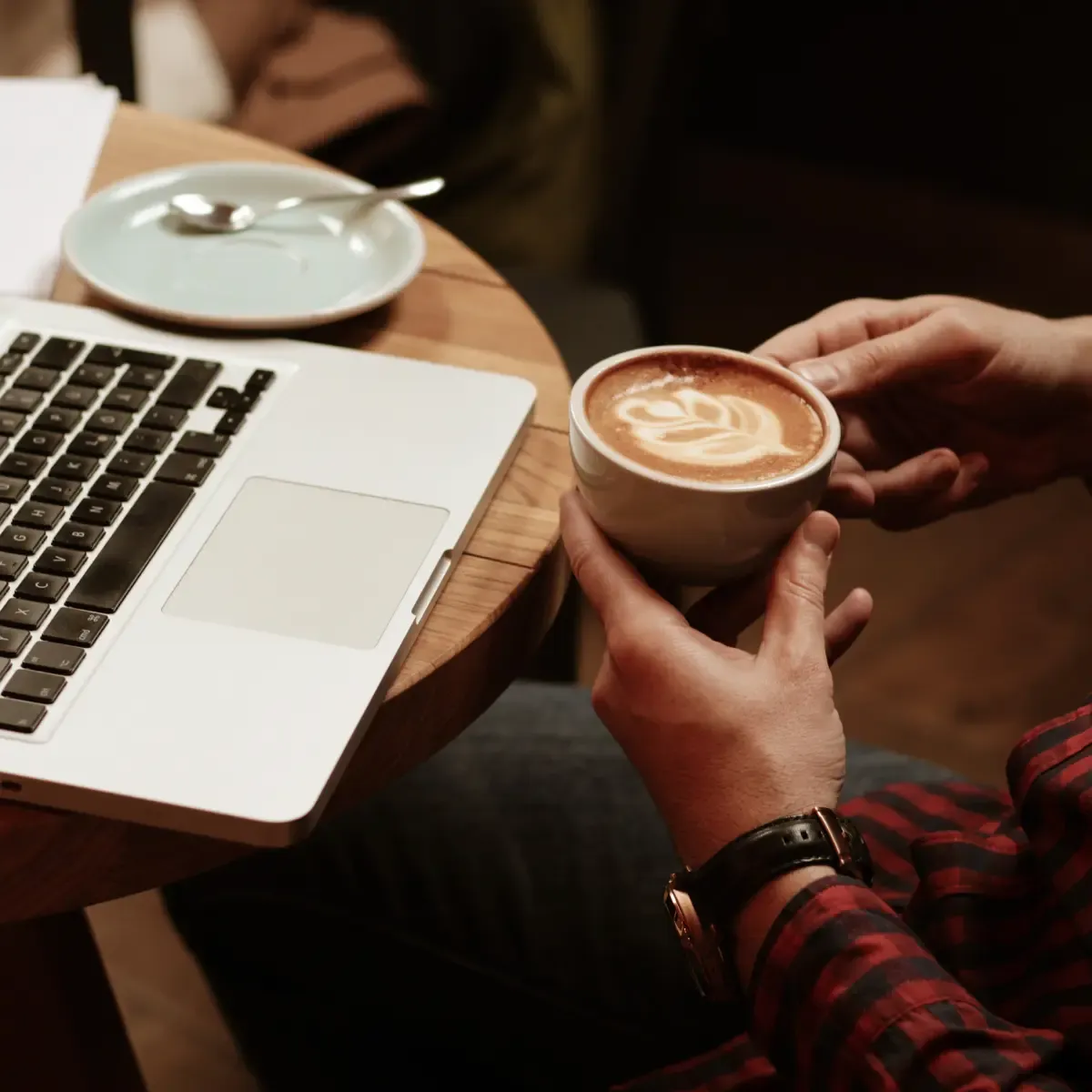 hands holding a cappucino by a laptop