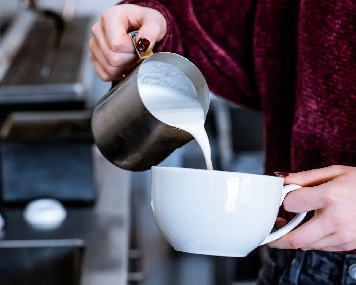 A hand pouring milk into a cup of coffee