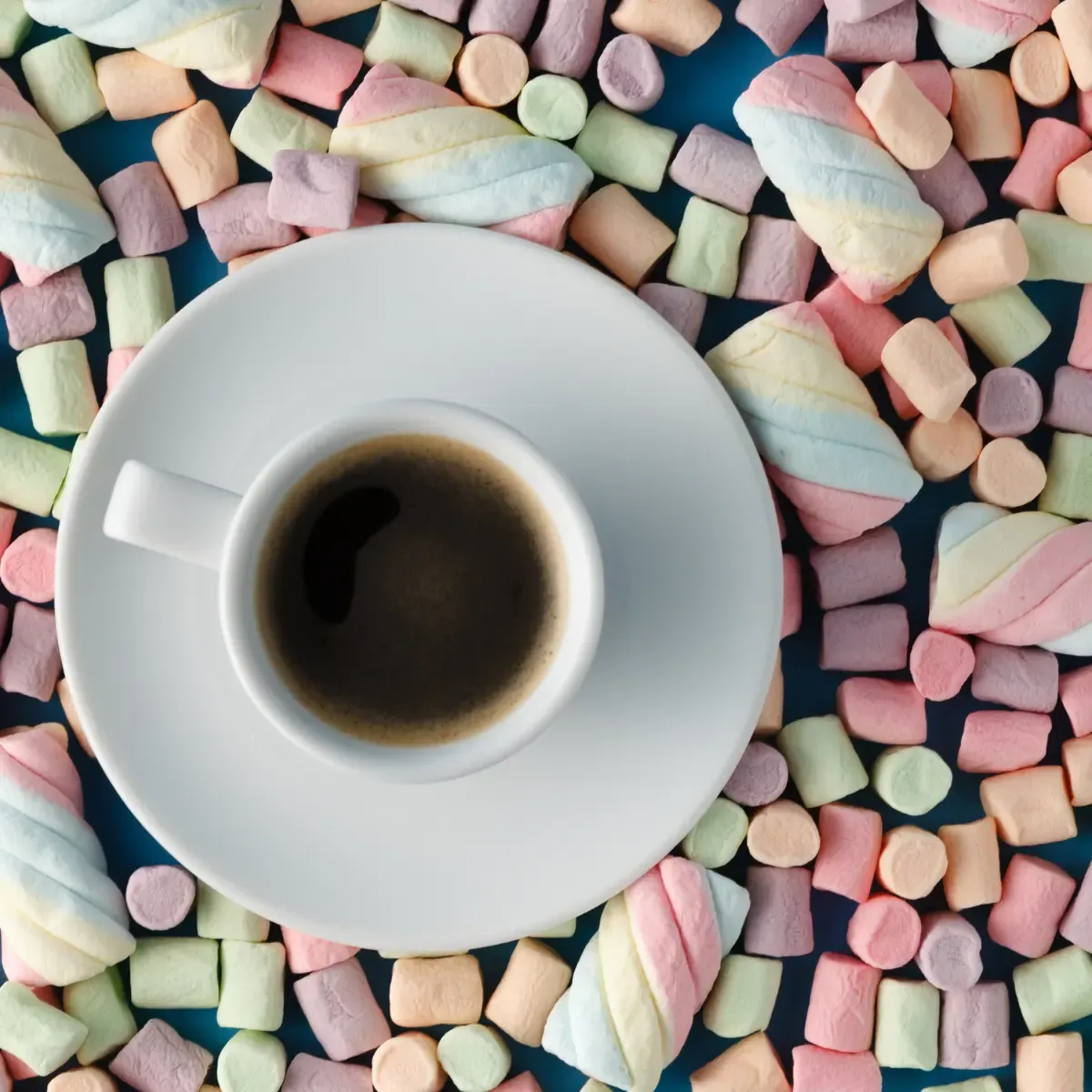 Multicolored marshmallows scattered around a cup of coffee
