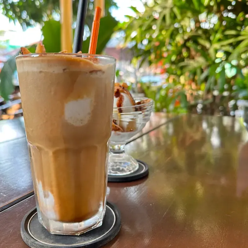 Café Dua - Coconut Espresso Frappé in a glass, plants in the background