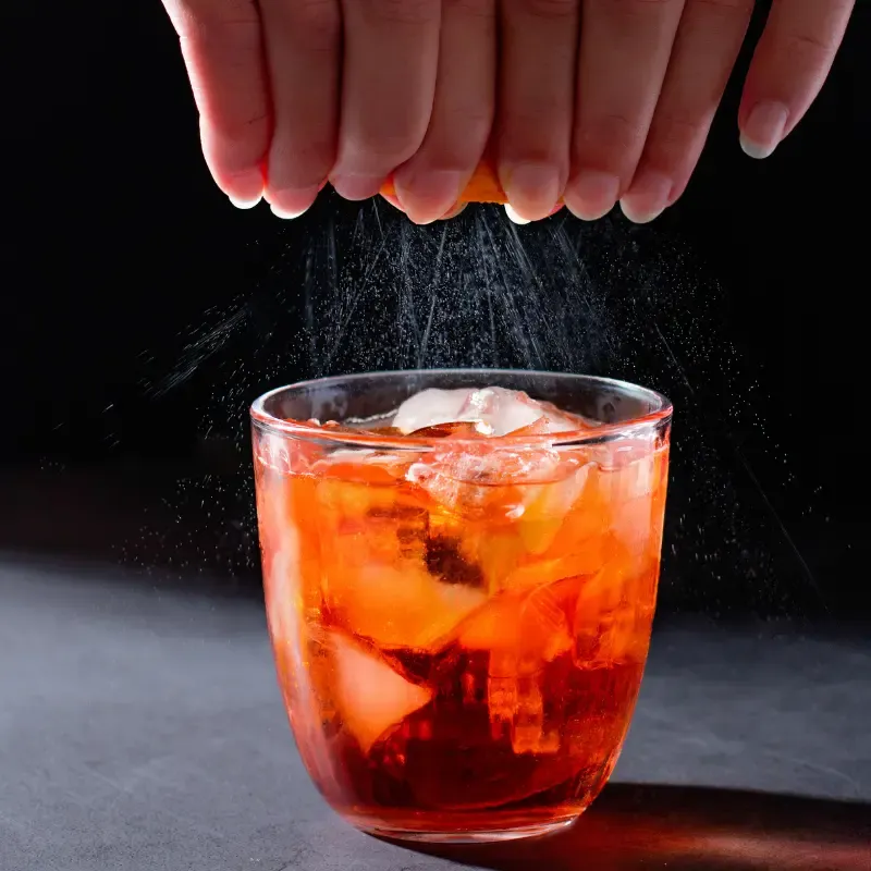 Hands squeezing an orange into a cold brew coffee