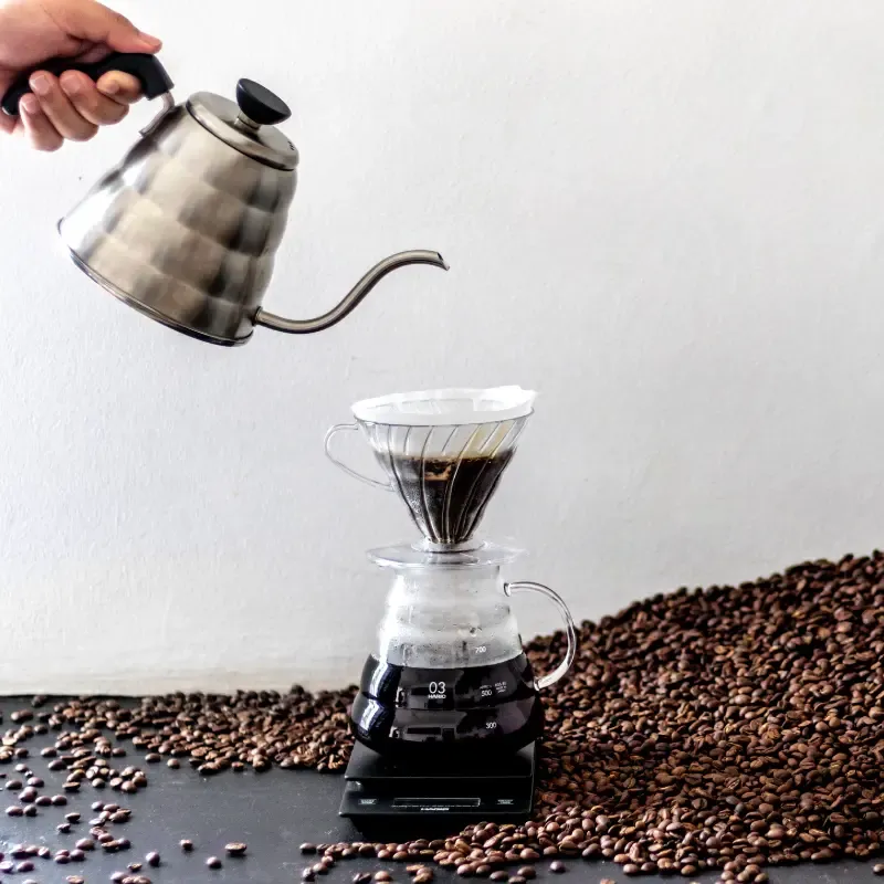 kettle pouring boiled water over coffee beans in a conical filter