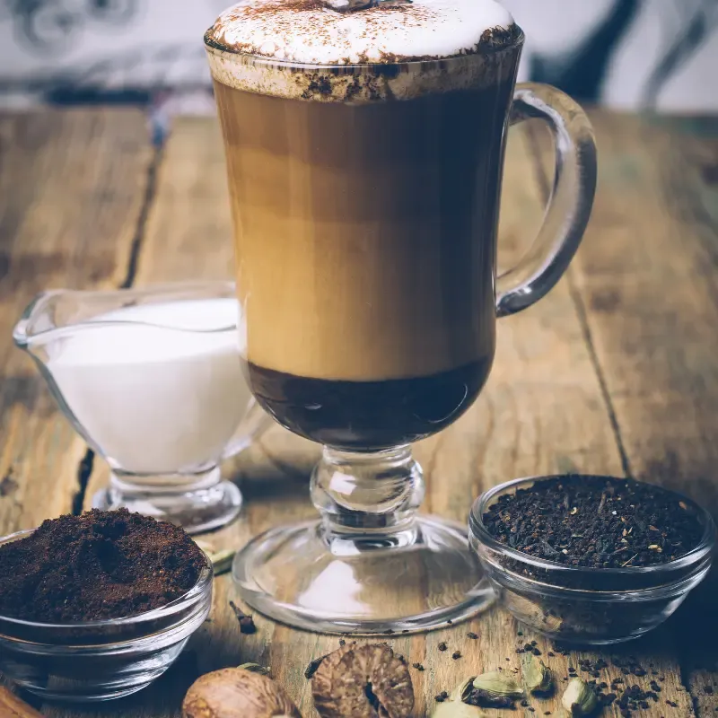 Chai coffee in a glass cup with spices, milk, coffee and tea