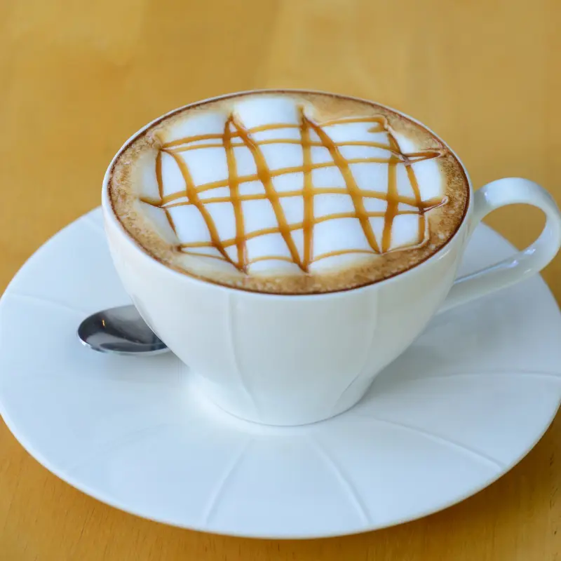 A macchiato drink with caramel drizzle in a white cup