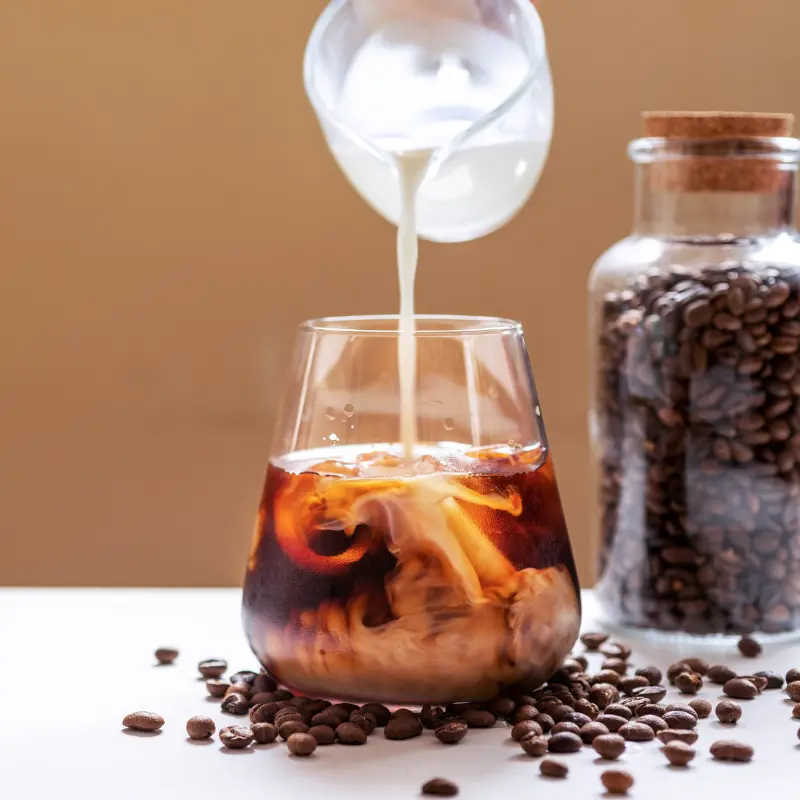 Pouring milk into a glass of cold brew coffee