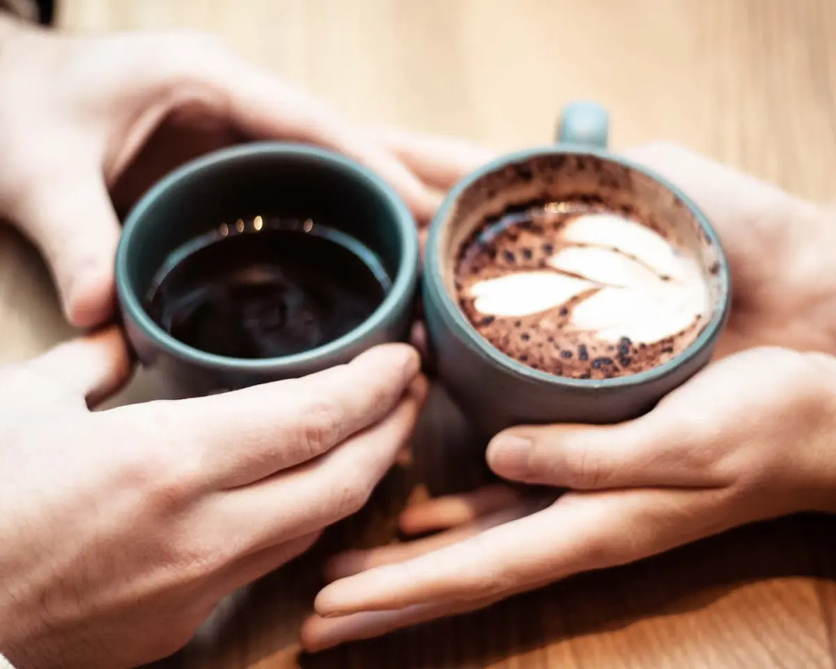 two cups of coffee holded by pairs of hands