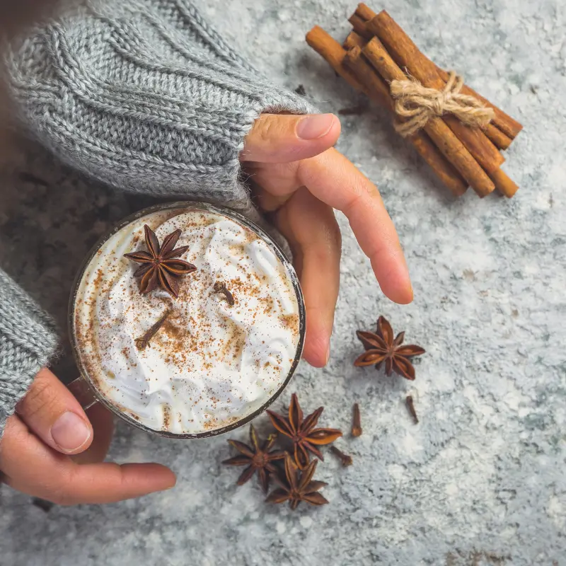 hands holding a cup of Chai Coffee with cinnamon sticks
