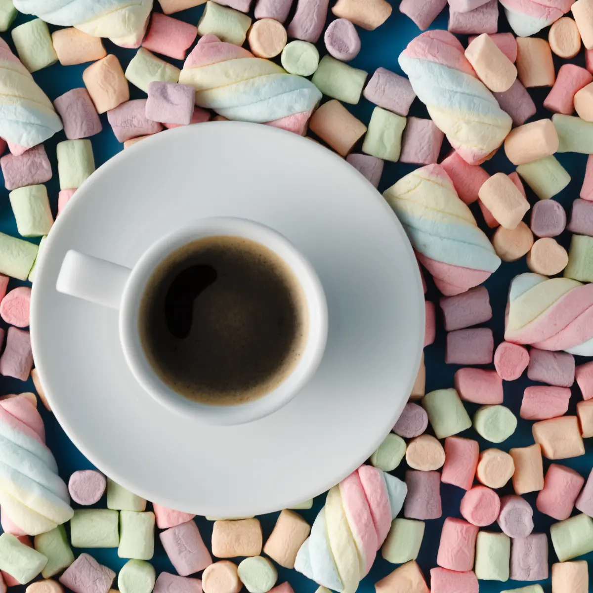 Multicolored marshmallows scattered around a cup of coffee