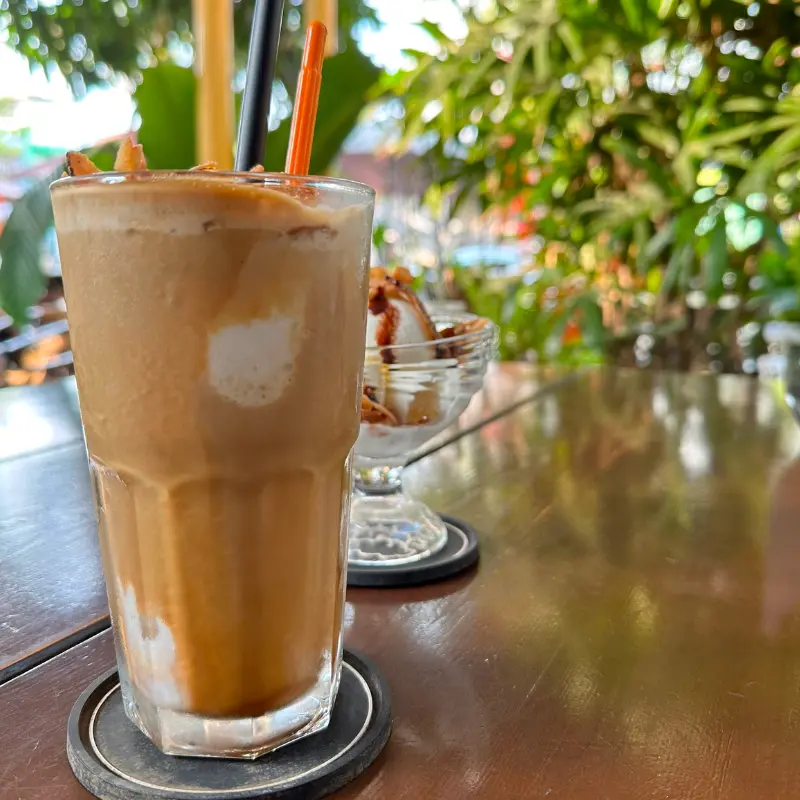 Café Dua - Coconut Espresso Frappé in a glass, plants in the background