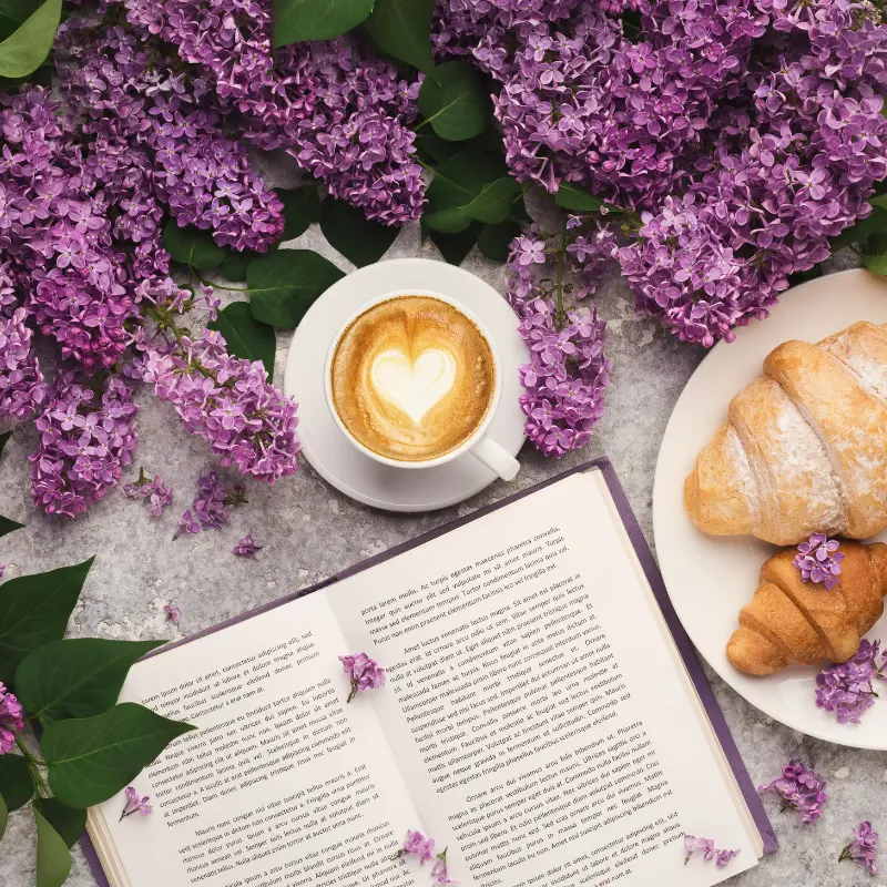 Spring Coffee Drinks with lilac flowers, a book and a croissant