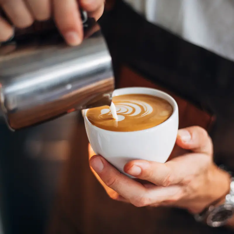 Latte art - a hand pouring froth milk into a cup of espresso